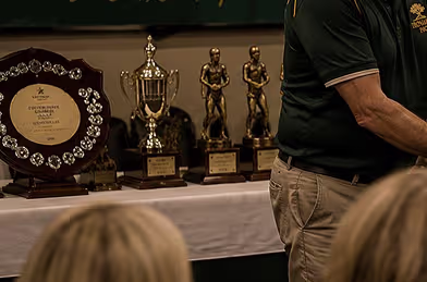 Engraved plates on the trophies and perpetual shield at the end of the awards table, medals laid out in front of them.